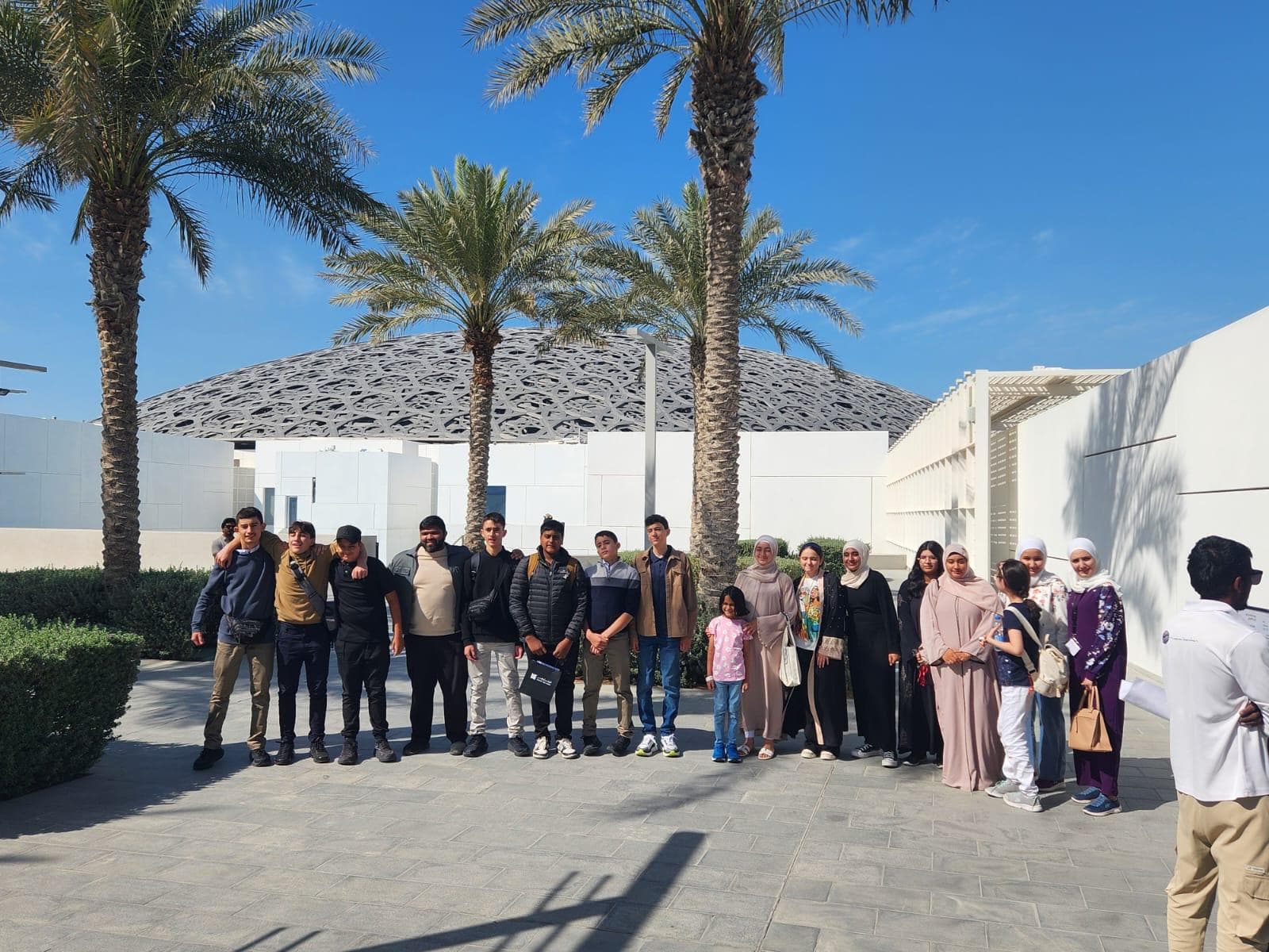 The group lined up under palm trees outside the Louvre Abu Dhabi dome