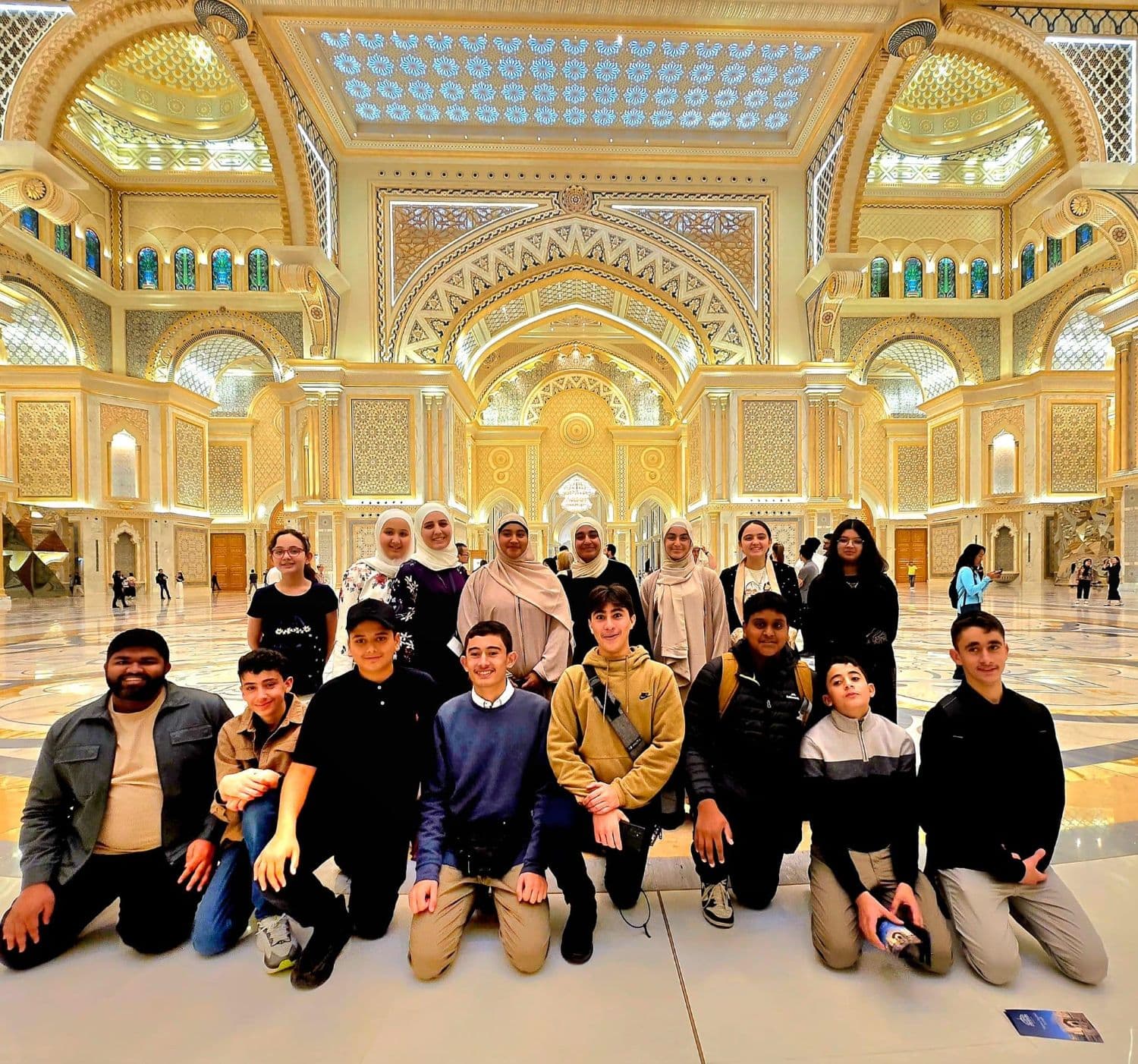 Students and leaders kneeling together in the grand hall of Qasr Al Watan